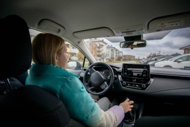 Bir kadın, şehir manzarasının ortasındaki modern ve şık iç tasarımı vurgularken ustaca araba kullanıyor.