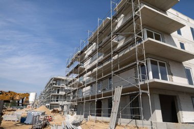 Yeni bir çok katlı bina yapım aşamasında. İskelesi görünür ve berrak mavi gökyüzü var.