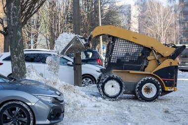 Ağır makineler yoğun bir kış manzarasında birikmiş karı büyük bir otoparktan çıkarmak için özenle çalışır.