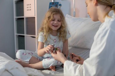 Sıcak bir hastane odasında, genç bir kız neşeyle ışıldıyor. Yanında ilgilenen bir bakıcı ile iletişim kurarken.