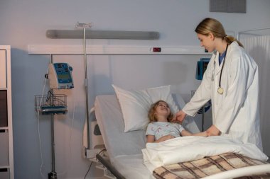 Bir hastane odasında, kendini adamış bir doktor iyileşme sürecinde olan genç bir hastayı dikkatle kontrol eder.