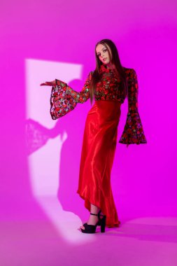 Şık bir model, kendine güvenerek şık pembe bir ortamda güzel çiçekli kolları olan koyu kırmızı bir elbise sergiliyor.