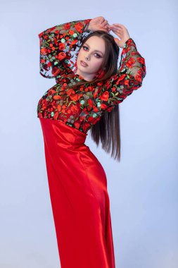 Zarif bir manken, karmaşık çiçek desenli, entelektüel ve tarz saçan canlı kırmızı bir elbise sergiliyor.