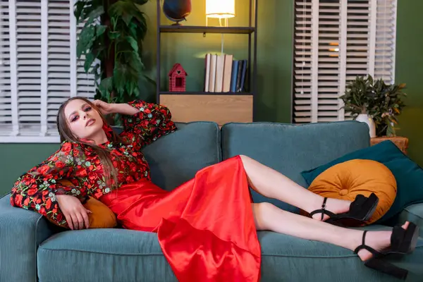 Bir model şık bir koltukta şık kırmızı bir elbise ve güzel bir çiçekli gömlek giyer.