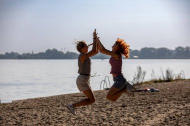 İki arkadaş sevinçle havaya sıçrayıp, güneşli bir günün tadını çıkarıyorlar.