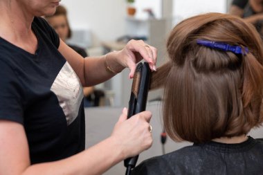 Parlak, modern bir salon ortamında düz ütü kullanarak saçı yaratıcı bir şekilde dönüştüren profesyonel bir stilist.