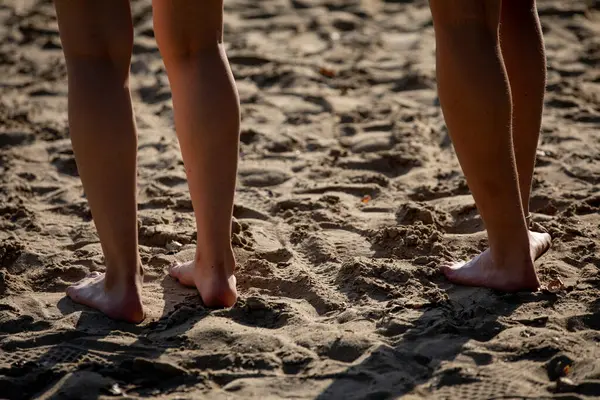 İki çift çıplak ayak, sıcak kumlu sahilde durup doğadaki bu unutulmaz anı kucaklıyor.