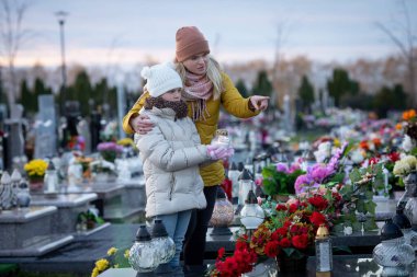 Mezarlıktaki bir anne ve çocuk arasında dokunaklı bir an. Sevdiklerini çiçeklerle ve anılarla onurlandırmak.