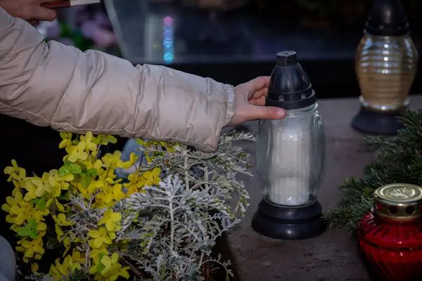 Nazik bir el, açık hava ortamında çeşitli canlı çiçekler arasında parlayan bir fenere uzanır.