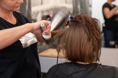 Yoğun bir kuaförde, yetenekli bir stilist müşterilere mükemmel saç stili yaratmak için saç kurutma makinesi kullanır.