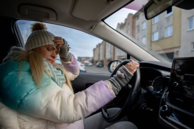 Kışlık giysiler içindeki bir kadın, soğuk havaya rağmen şehrin canlı yaşamını yansıtan arabasını kullanır.