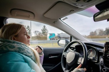 Mavi paltolu bir kadın, dışarıdaki soğuk havaya göğüs gererken sürekli olarak otoyolda araba kullanır.