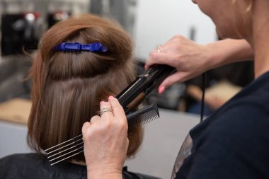 Profesyonel bir kuaför, müşterilerinin saçlarını parlak ve parlak göstermek için ütüyü ustalıkla kullanır.