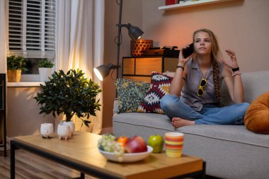 Oturma odasında lezzetli atıştırmalıklarla çevrili bir kadın evinde telefonla mutlu bir şekilde eğleniyor.