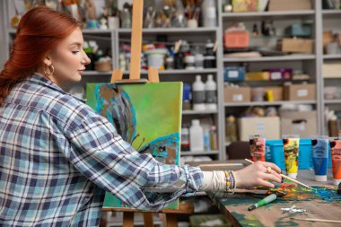 Genç ve hevesli bir sanatçı, çeşitli sanat malzemeleriyle dolu parlak ve renkli bir stüdyoda neşe içinde resim yapıyor.