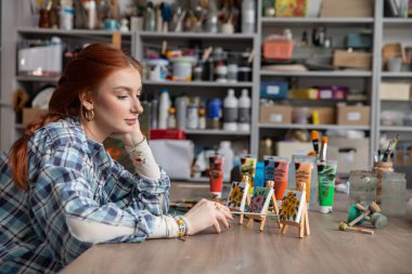 Odaklanmış ve kendini işine adamış bir sanatçı canlı stüdyosundaki renkli, canlı minyatür sanat eserlerini dikkatle değerlendiriyor.
