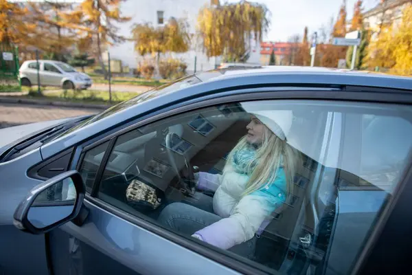 Sıcak kış kıyafetleri giymiş genç bir kız harika bir sonbahar gününde bir arabanın içinde rahatça oturuyor.