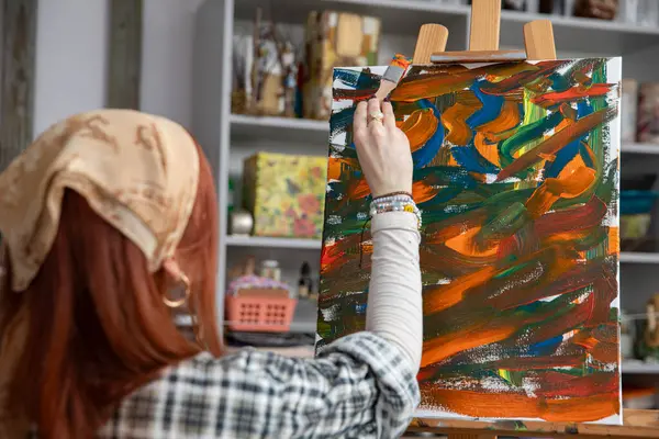 Bir sanatçı, renkli stüdyo alanlarında canlı ve soyut bir tablo yaratmakla tutkuyla meşguldür.