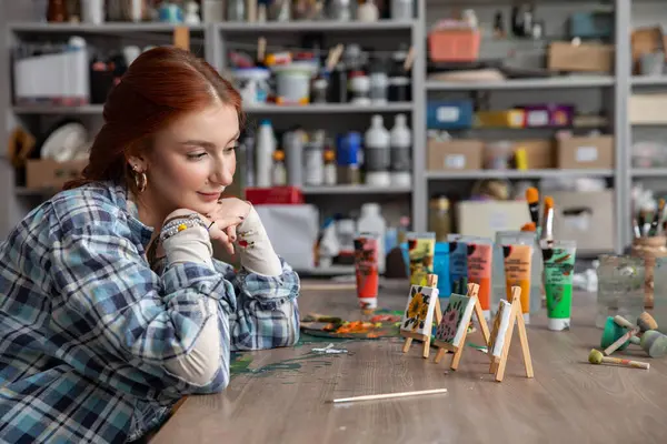 Malzemelerle dolu canlı bir sanat stüdyosunda, düşünceli genç bir kadın güzel sanat eserlerine hayranlık duyuyor ve yansıtıyor.