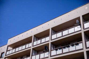 Çağdaş bir apartman manzarası canlı mavi bir gökyüzünün altında, parmaklıklı balkonları gösteriyor..