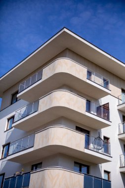 Çağdaş bir apartman kompleksi. Açık mavi gökyüzünün altında parlak çizgiler ve geniş balkonlar var..