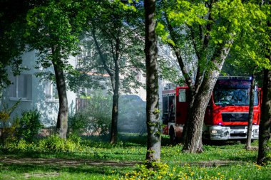 Bir itfaiye aracı, ağaçlarla çevrili bir evin yakınına park edilir ve acil bir durum söz konusudur.