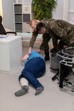 Yaralı bir insana gerçekçi bir eğitim senaryosunda yardım eden askeri personeli gösteren detaylı bir sahne.