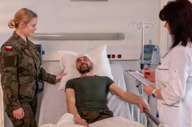 Doktor durumu değerlendirirken, askeri bir üye hastaya destek ve rahatlık sunar.