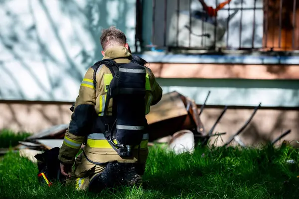 Cesur bir itfaiyeci binanın yakınındaki çimlerin üzerine diz çöker ve acil bir duruma müdahale eder.