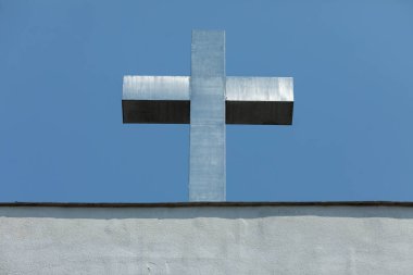 Çarpıcı bir gümüş haç belirgin bir şekilde parlak mavi gökyüzüne karşı duruyor, derin inanç ve maneviyatı temsil ediyor.