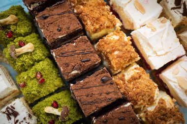 Baklava kareleri ve çeşitli kremalı tatlılar içeren canlı ve renkli bir tatlı çeşidi.