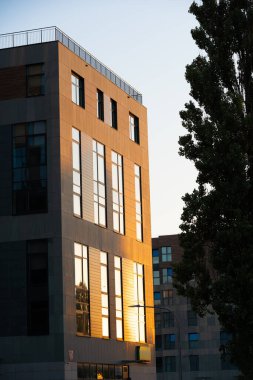 Şık, modern bir bina hareketli bir şehir manzarasında gün batımının canlı renklerini parlak bir şekilde yansıtıyor.