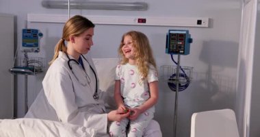 Şefkatli bir doktor hastane odasında bir çocukla sevgi dolu bir şekilde iletişim kurarak hem rahatlığı hem de güveni arttırır.
