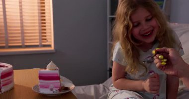 Genç bir kız, sevgi, neşe ve mutlulukla çevrili rahat yatağında lezzetli pembe bir pastanın tadını çıkartıyor.