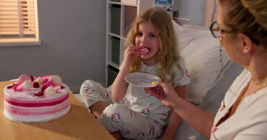 Genç bir kız, bakıcısıyla birlikte hastanede pastanın tadını çıkarıyor. İyileşme sürecinde neşeli anlar yaşıyor.