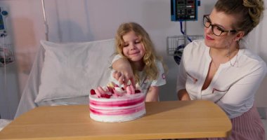 Neşeli bir hastane ortamında bir yetişkinle pastanın keyfini çıkaran bir çocuğun iç açıcı ve keyifli bir sahnesi.