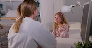 Pediatrik doktor, genç bir kızla sağlık hizmetleri ortamında sıcak bir şekilde iletişim kurarak onun rahatlığını ve güvenliğini sağlar.