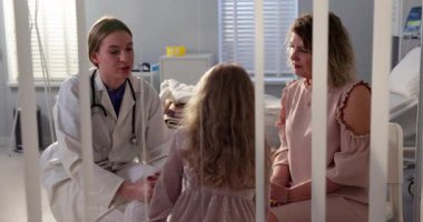 Bir hastane odasında, şefkatli bir doktor genç bir kız ve annesiyle yakınlaşır, şefkat ve empati gösterirler.