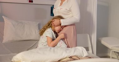 Bir hastane odasında, bir anne çocuğunu rahatlatır, bu zor anlarda muazzam bir sevgi ve destek gösterir.