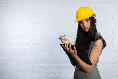 Sert bir şapka takan kendini işine adamış bir kadın işçi, hareketli bir inşaat alanında notlarını dikkatle inceler ve inceler.