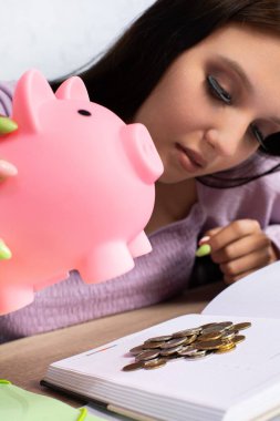 Kararlı bir genç, mali eğitimin önemini vurgulayarak, pembe bir kumbaradaki paraları inceliyor.
