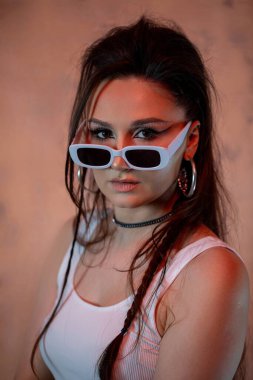 Şık güneş gözlükleriyle poz veren cesur genç bir kadın modern sokak tarzını sergiliyor.