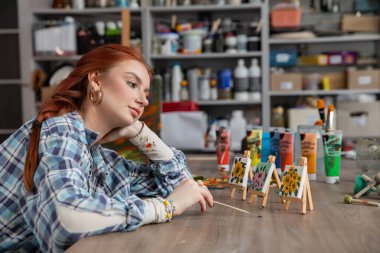 Son derece düşünceli bir sanatçı, yaratıcılığına tamamen dalmış canlı ve renkli eserlerine dikkatle bakar.