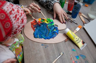 Genç eller heyecan verici ve canlı bir sanat projesiyle meşguller, palette çeşitli renkleri karıştırıyorlar.