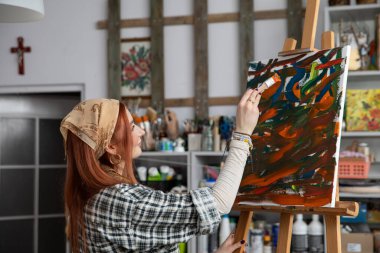 Parlak ve ilham verici bir sanat stüdyosu atmosferinde canlı ve renkli tablosuna derinden odaklanmış bir kadın.