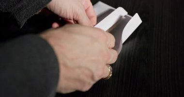 Bir kişi ihtiyatlı bir para transferinin gerçekleşmesini sağlamak için dikkatlice beyaz bir zarfa para yerleştiriyor.