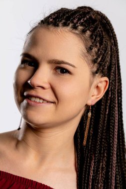 Saçları örgülü neşeli bir genç kadın, basit bir arkaplan karşısında kendine güvenini ve tarzını sergiliyor.
