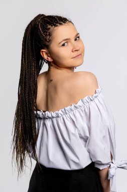 Şık bir genç kadın zarif pozlar veriyor, örgülü saçlarını ve modayı omuzlarından çıkarıp kendine güveni yayıyor.