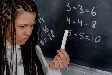 Düşünceli bir öğrenci, akademik zorlukların vurgulandığı bir tahtada karmaşık matematik denklemleri okuyor.