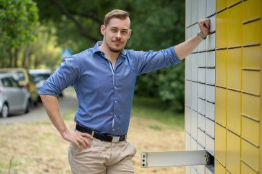 Şık bir genç adam, kendine güvenen bir şekilde çağdaş bir binanın yanında duruyor, renkli parlak bir gömlek giyiyor.